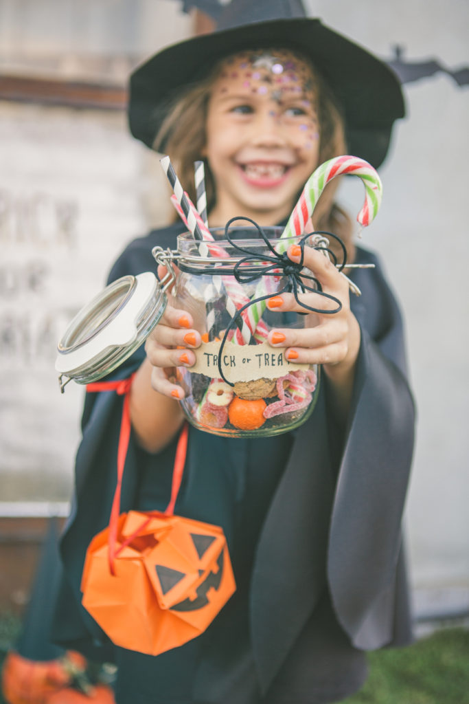 Cute girl dressed as a witch holding Halloween treats.